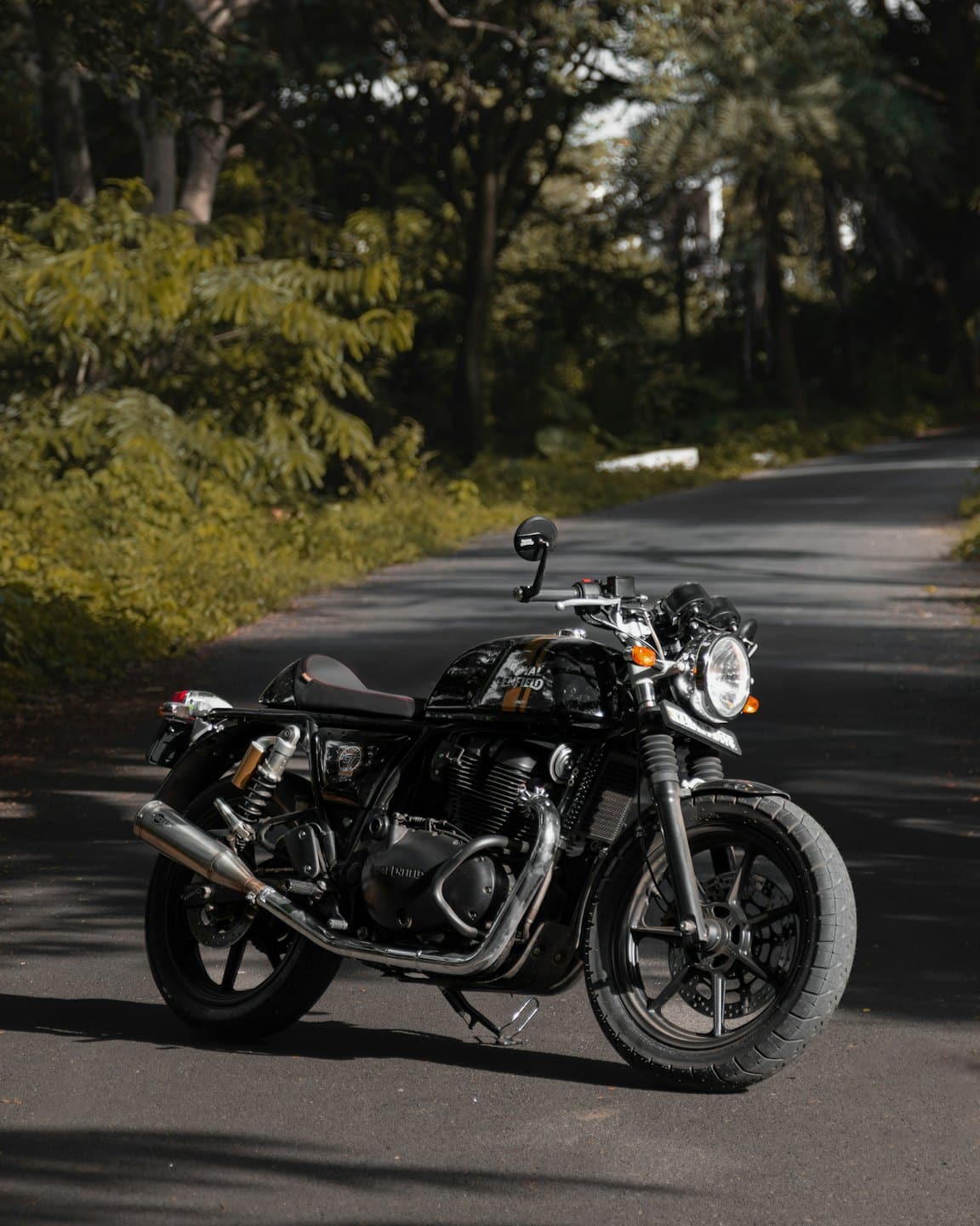 A black classic motorcycle parked on a shaded asphalt road.